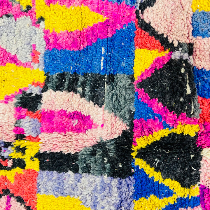 Vintage Moroccan rug with vibrant geometric patterns in pink, blue, yellow, and black, showcasing traditional Berber artistry.