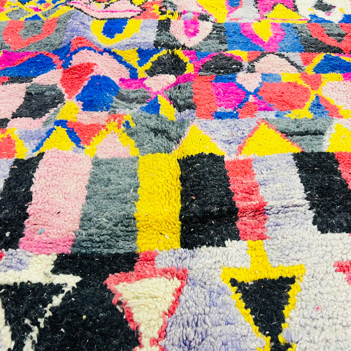 Vintage Moroccan rug with vibrant pink, yellow, blue, and black geometric patterns, showcasing Berber artistry and tribal motifs.
