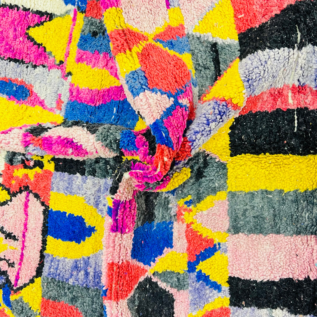 Close-up of vibrant vintage Moroccan rug with bold pink, yellow, blue, and black geometric patterns, showcasing Berber artistry.