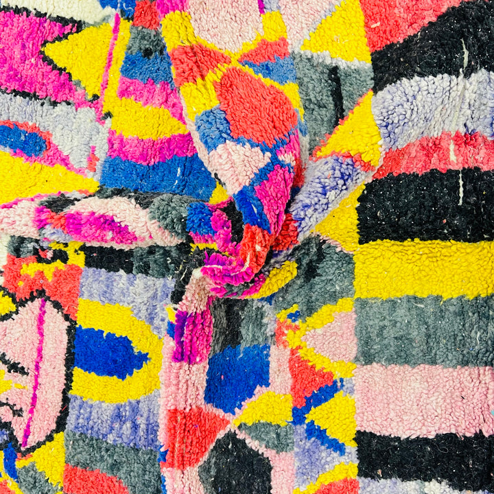 Close-up of vibrant vintage Moroccan rug with bold pink, yellow, blue, and black geometric patterns, showcasing Berber artistry.