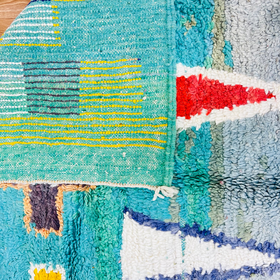 Vintage Moroccan rug featuring vibrant geometric motifs and traditional Berber weaving in turquoise, red, and yellow hues.