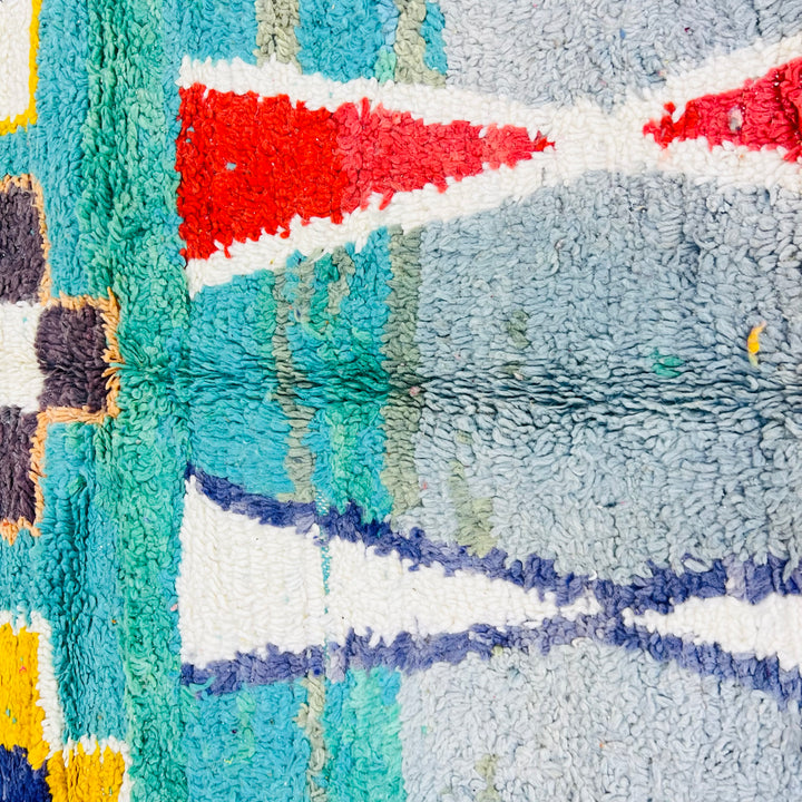 Close-up of a vintage Moroccan rug with vibrant geometric patterns in turquoise, red, yellow, and violet. Moroccan wool rug detail.