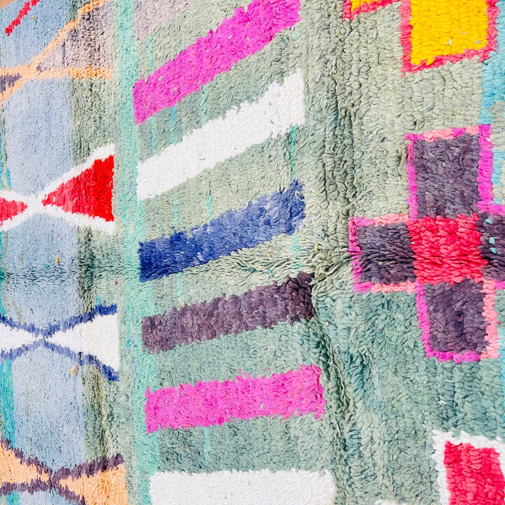 Colorful geometric patterns on a vintage Moroccan rug with pink, blue, and red designs, handmade using traditional Berber techniques.