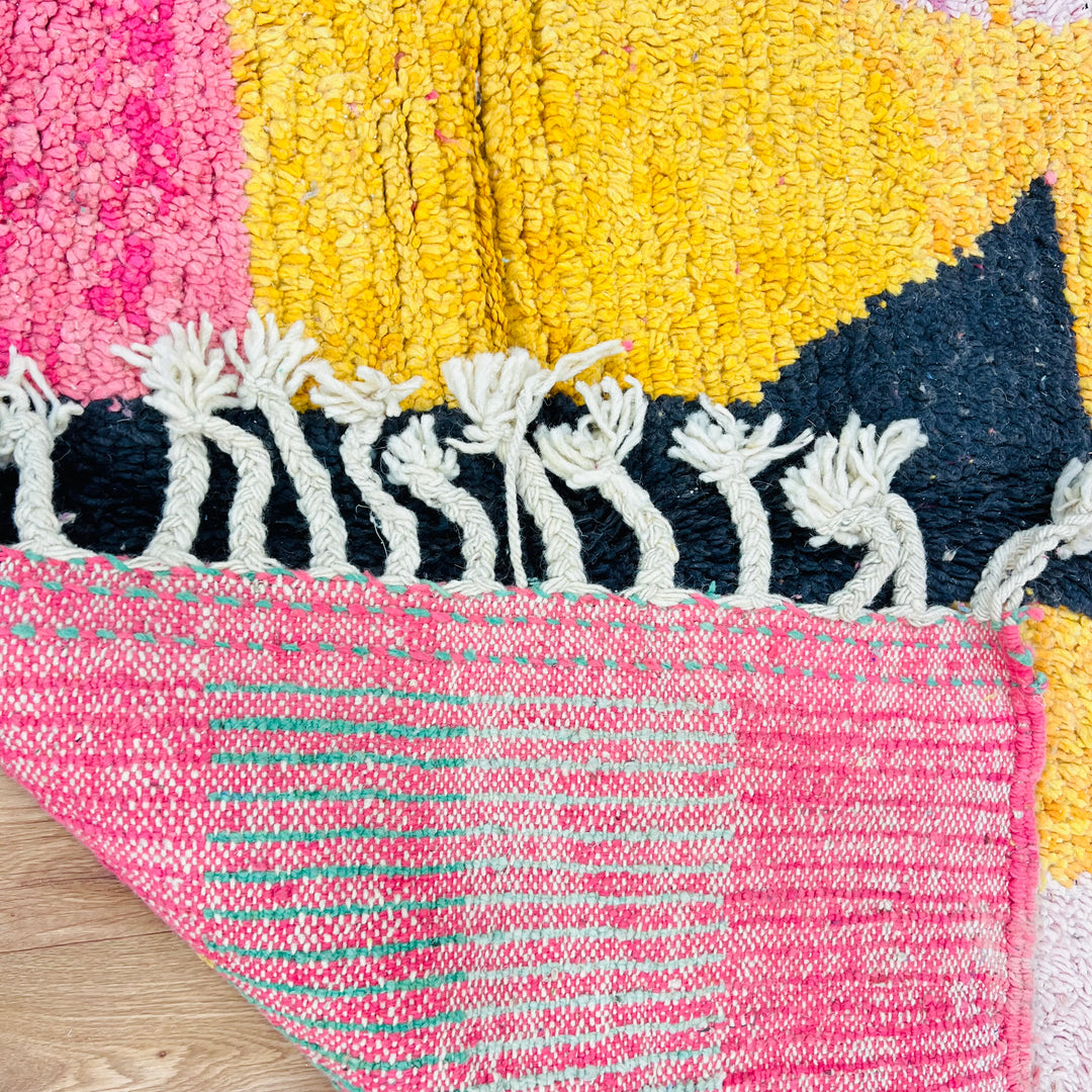 Colorful vintage Moroccan rug with pink, yellow, and black abstract design, showcasing Berber symbolism and fringe details.