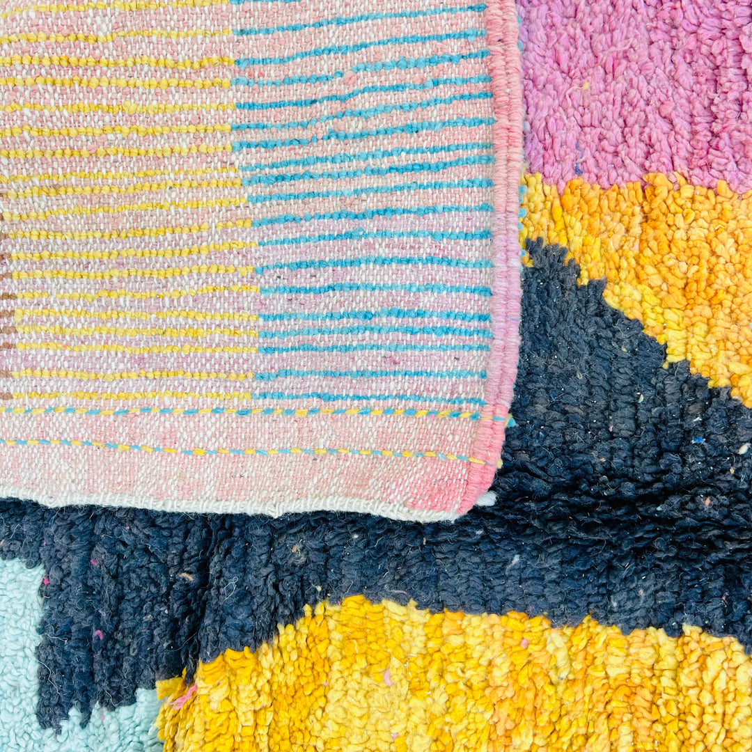 Colorful vintage Moroccan rug with bold stripes and central black abstract pattern, featuring pink, yellow, and turquoise accents.