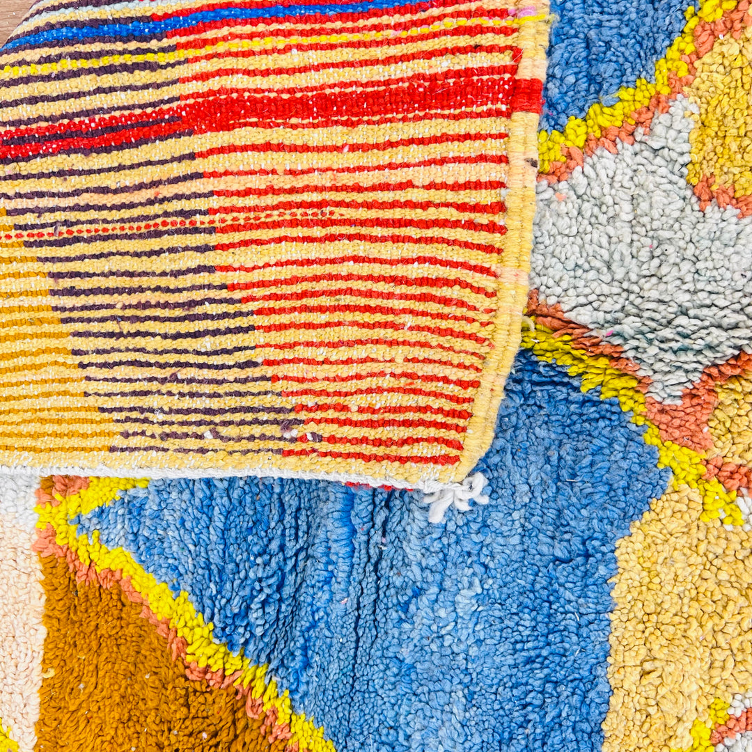 Close-up of a colorful vintage Moroccan Berber rug with blue, yellow, and red patterns. Handwoven wool carpet, traditional craftsmanship.