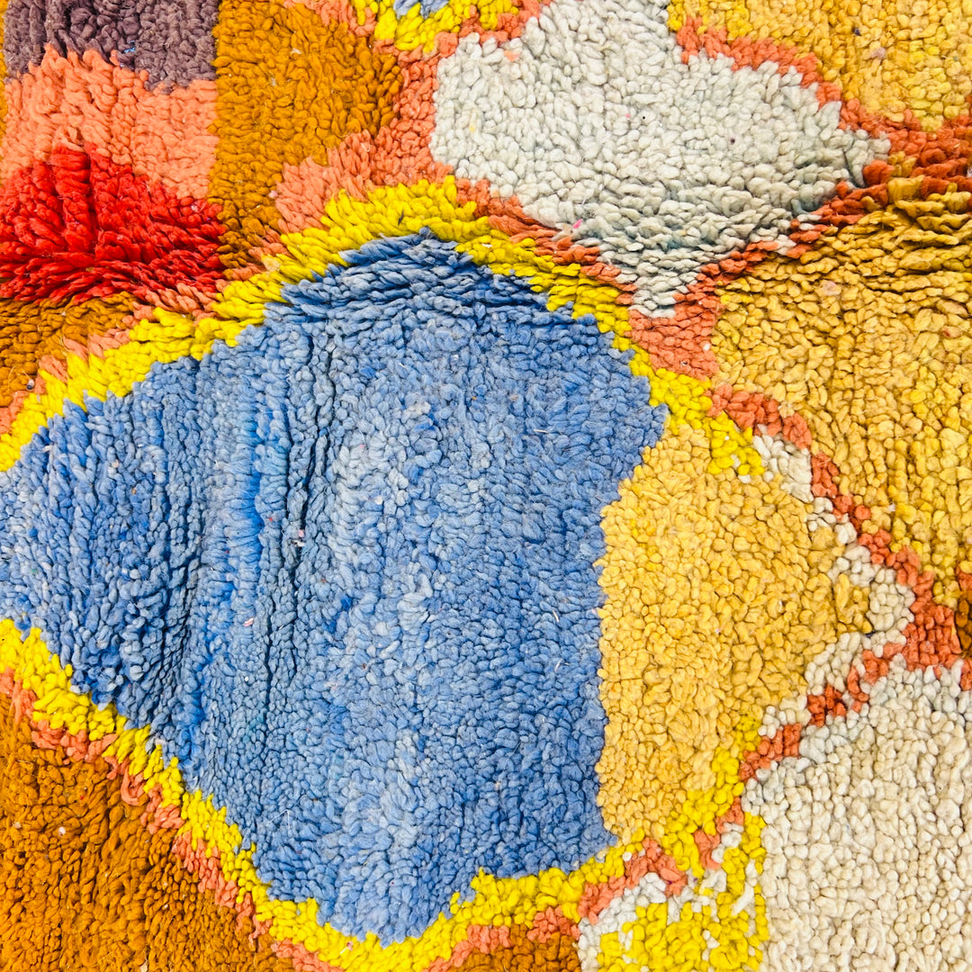 Vintage Moroccan rug close-up with blue diamond motif and earthy tones, showcasing traditional Berber craftsmanship.