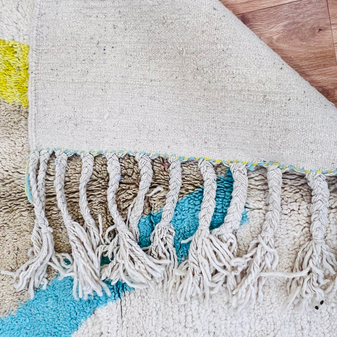 Handmade vintage Moroccan wool rug with fringes and blue and yellow diamond pattern on ivory background.