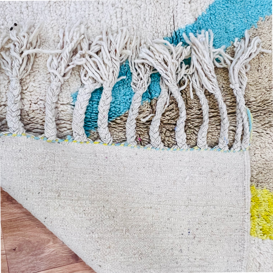 Close-up of vintage Moroccan rug with wool fringe, showcasing blue and yellow diamond design, emphasizing Berber craftsmanship.