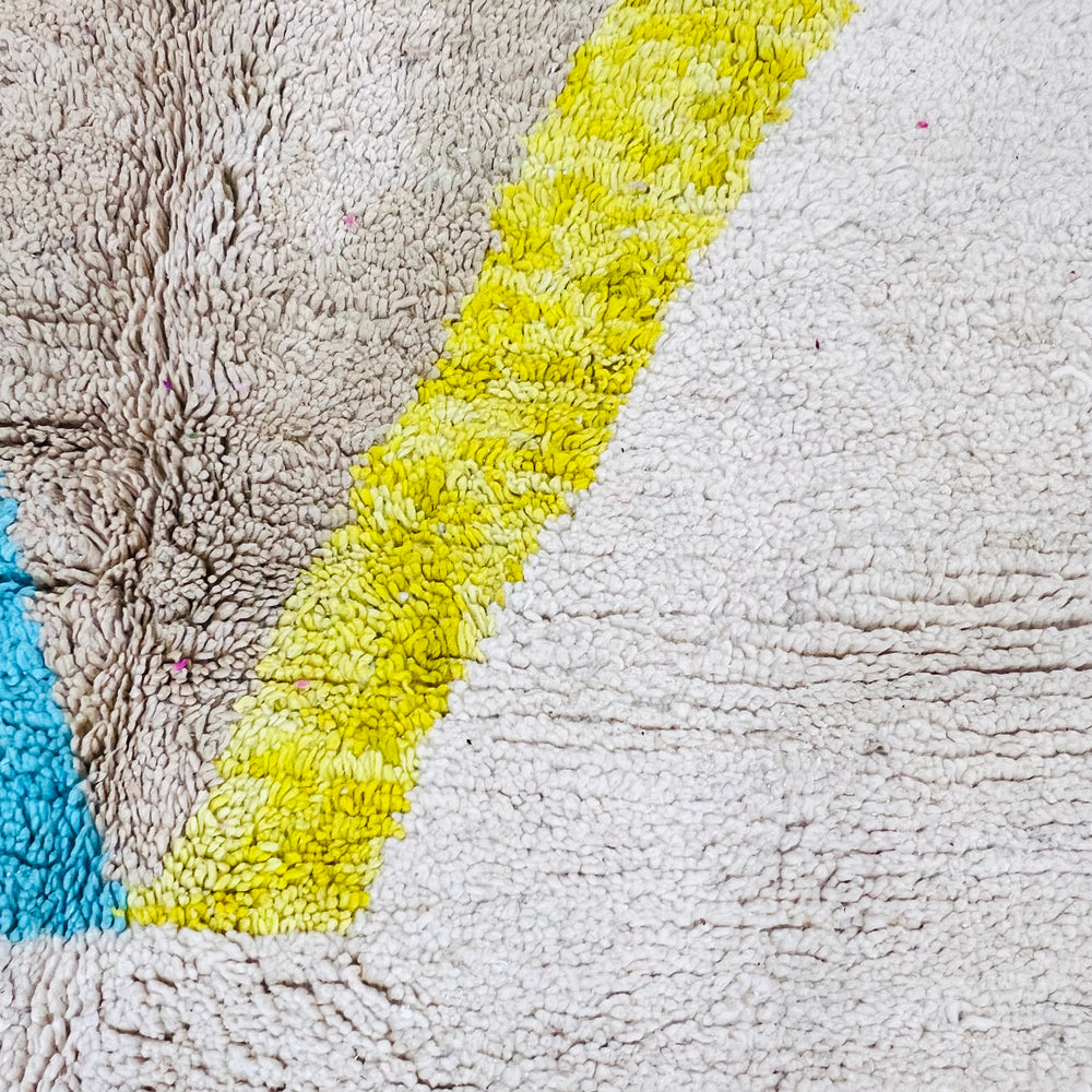 Close-up of a vintage Moroccan rug with abstract diamond patterns in earthy brown, sky blue, and sunshine yellow on an ivory backdrop.