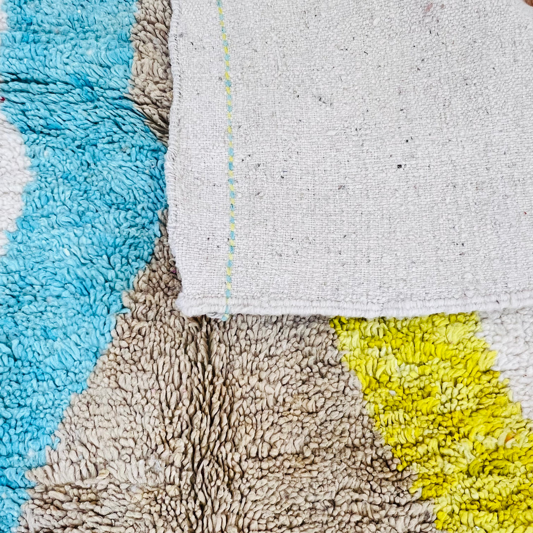 Close-up of a vintage Moroccan Berber rug with abstract diamond design in blue, yellow, and brown on an ivory background.