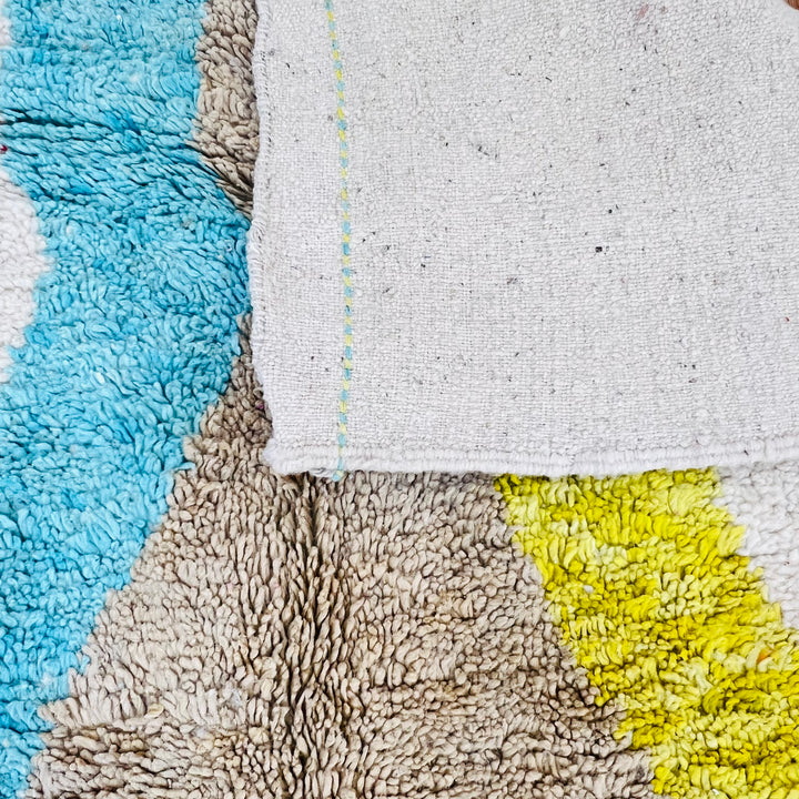 Close-up of a vintage Moroccan Berber rug with abstract diamond design in blue, yellow, and brown on an ivory background.