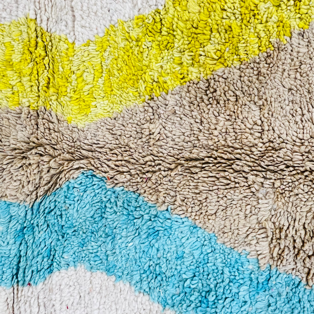 Close-up of a minimalist vintage Moroccan rug with diamond patterns in brown, blue, and yellow on an ivory wool background.