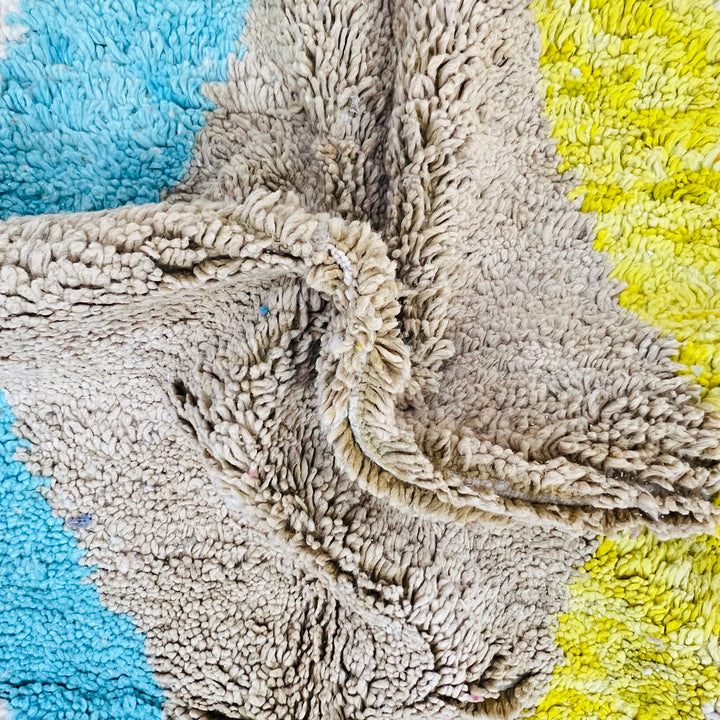 Close-up of a colorful Moroccan wool rug with blue, yellow, and beige shag textures, showcasing traditional Berber craftsmanship.