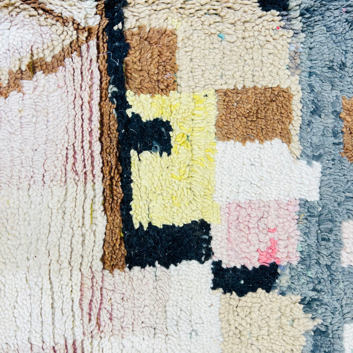 Close-up of a vintage Moroccan rug with geometric patterns in pink, brown, yellow, and ivory, showcasing Berber craftsmanship.