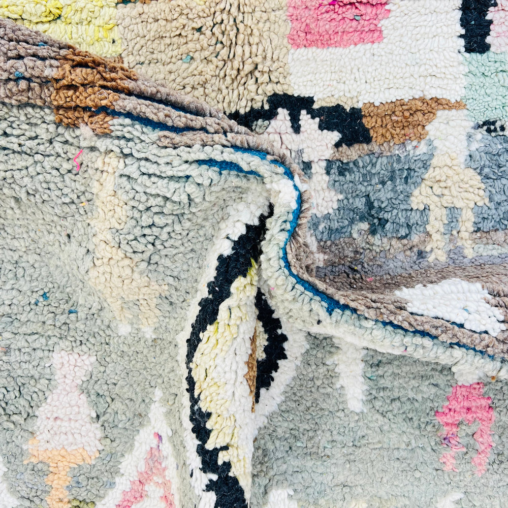 Close-up of vintage Moroccan Berber rug with geometric patterns in green, pink, and ivory – handmade artisan textile.