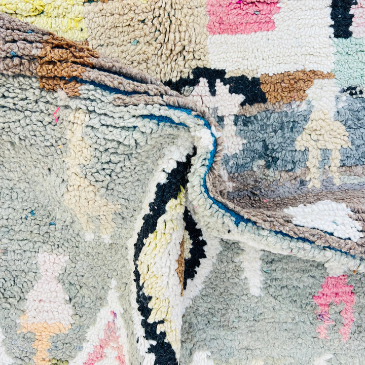 Close-up of vintage Moroccan Berber rug with geometric patterns in green, pink, and ivory – handmade artisan textile.