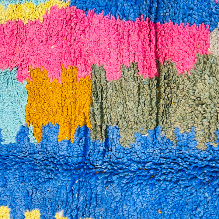 Colorful vintage Moroccan rug with abstract patterns in pink, orange, blue, and green, showcasing Berber craftsmanship and wool texture.