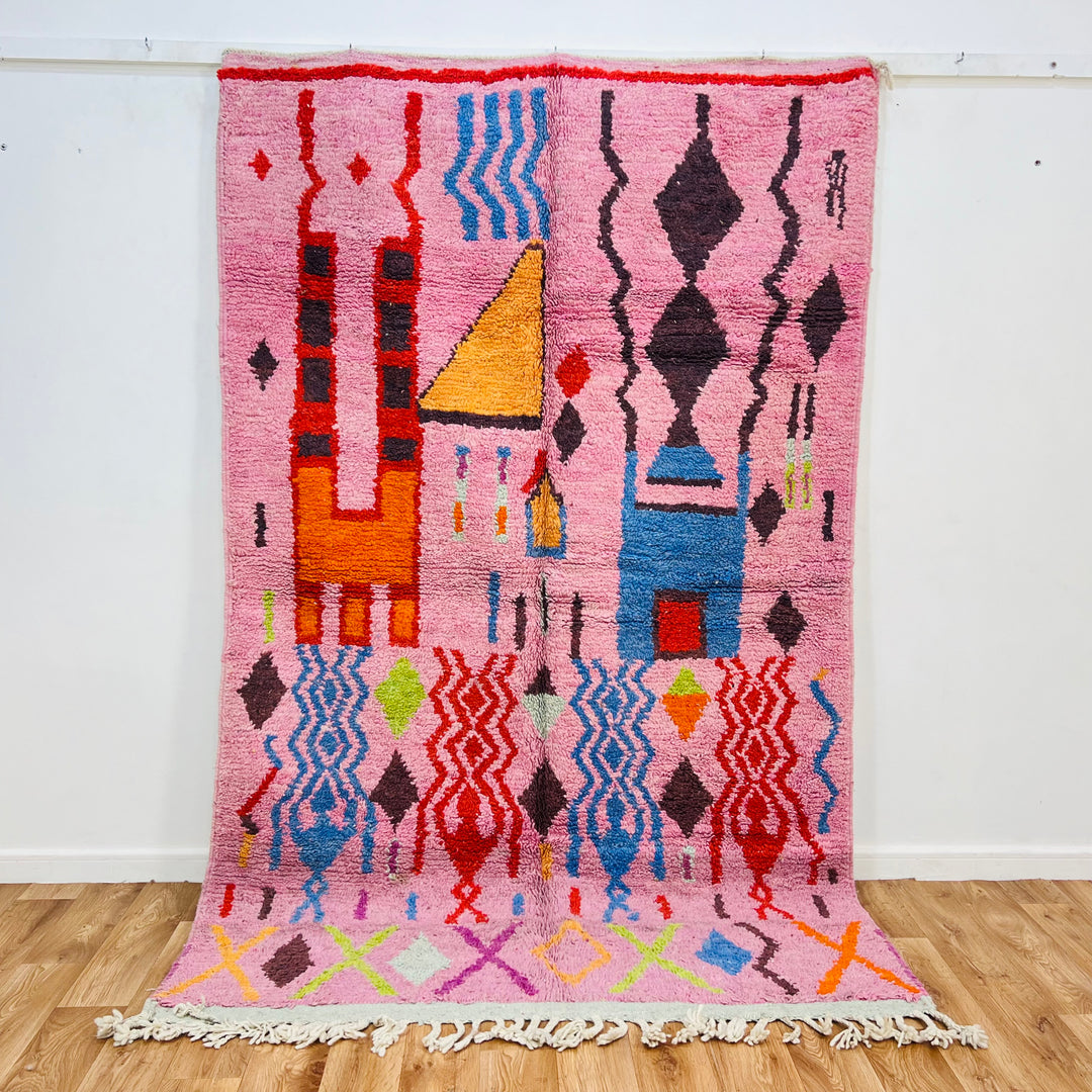 Pink vintage Moroccan rug with geometric Berber motifs in red, orange, blue, green, and yellow. Handwoven wool, 246 x 157 cm.