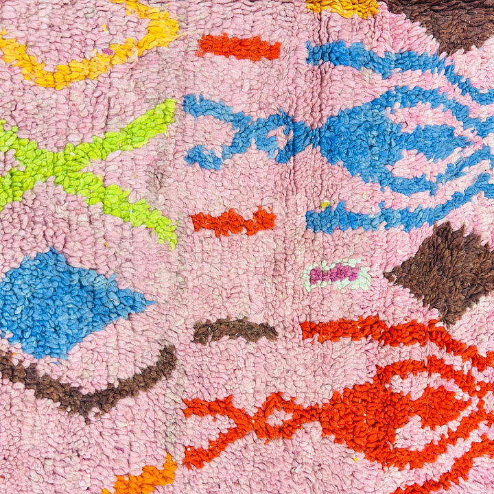 Pink vintage Moroccan rug with colorful geometric Berber motifs in red, orange, blue, green, and yellow on a wool texture.