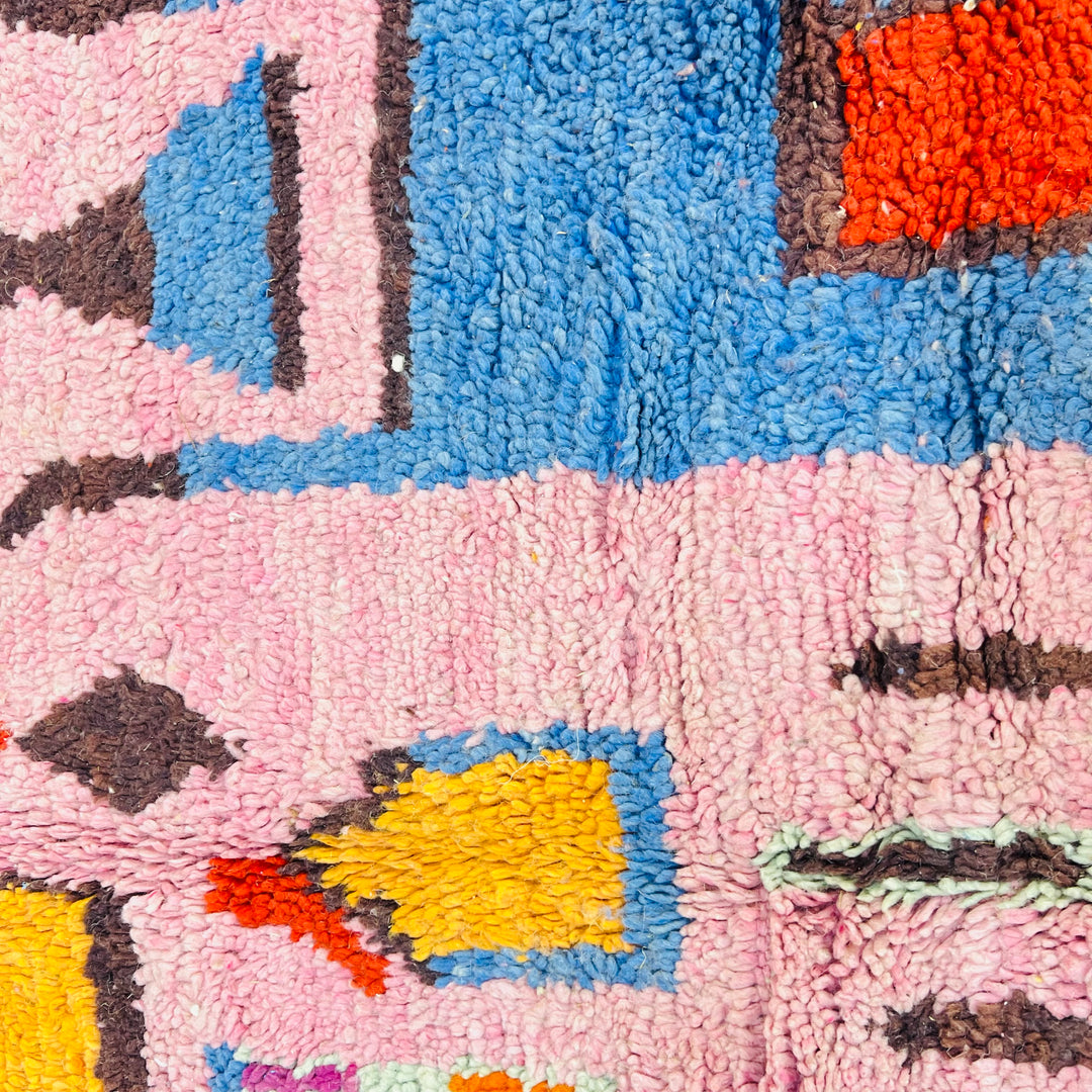 Close-up of a pink vintage Moroccan rug with geometric Berber motifs in red, orange, blue, and yellow. Handwoven wool design.