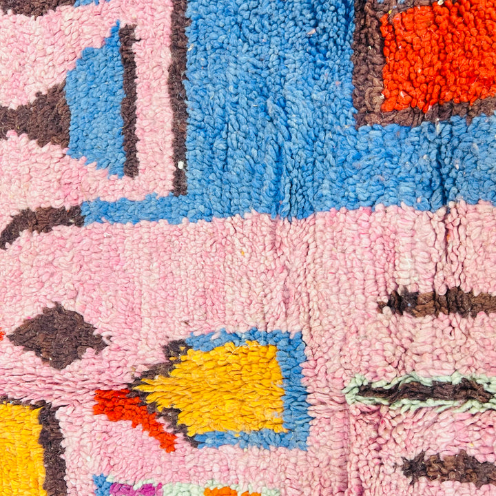 Close-up of a pink vintage Moroccan rug with geometric Berber motifs in red, orange, blue, and yellow. Handwoven wool design.