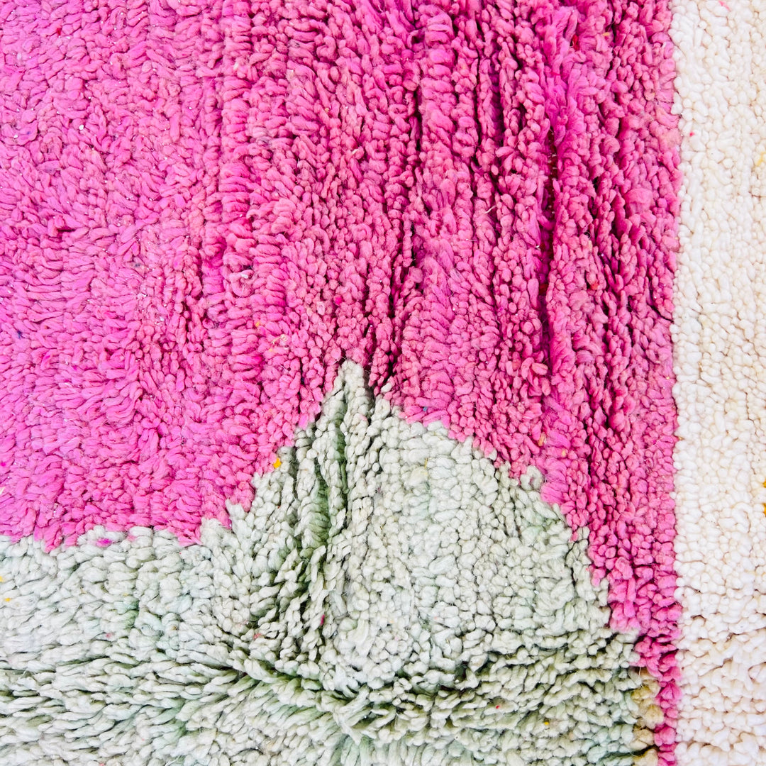 Close-up of a vintage Moroccan wool rug in pink and sage green showing abstract geometric patterns. Handmade Berber craftsmanship.