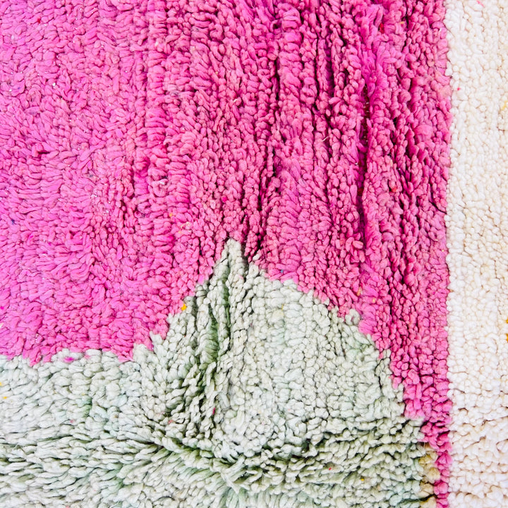 Close-up of a vintage Moroccan wool rug in pink and sage green showing abstract geometric patterns. Handmade Berber craftsmanship.