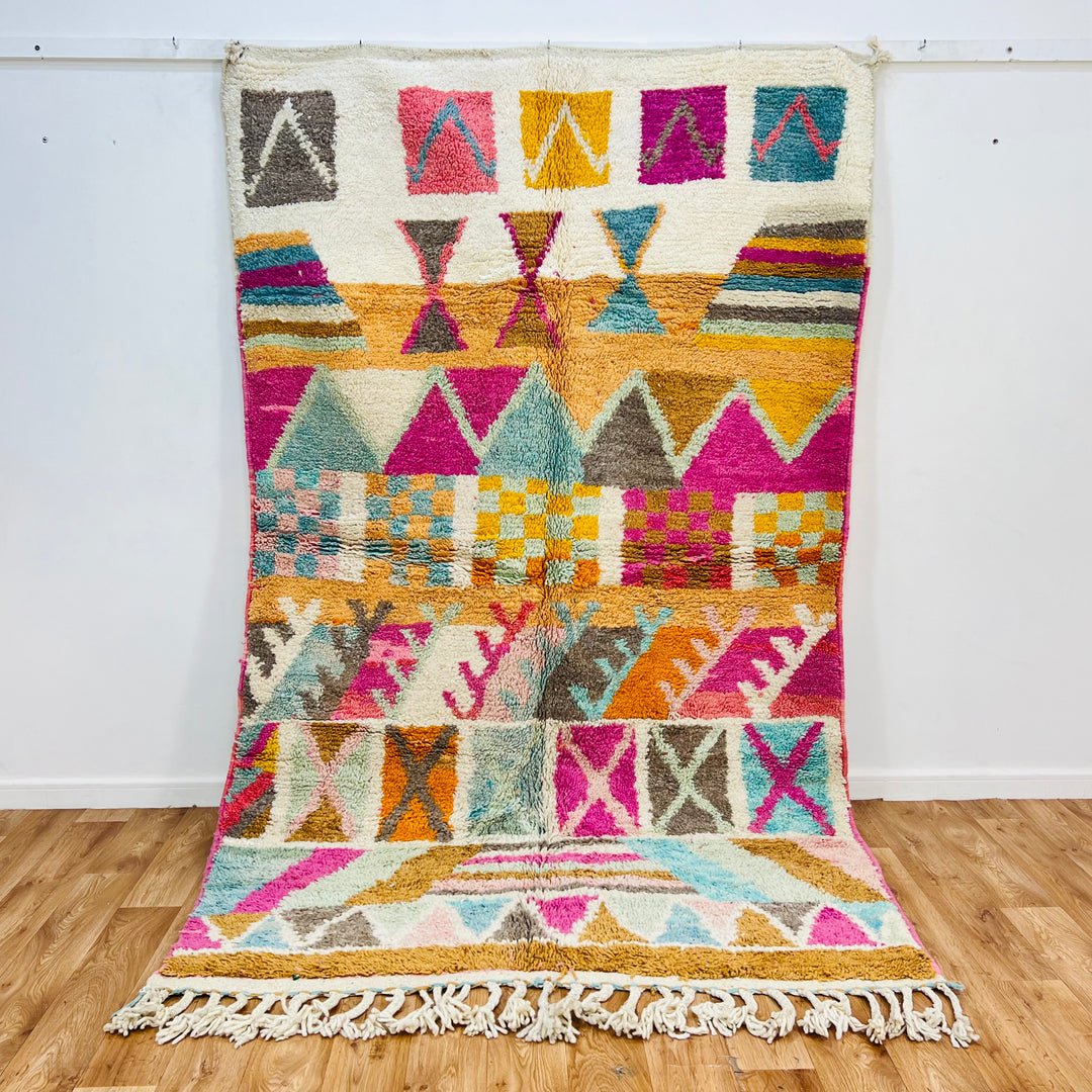Colorful vintage Moroccan rug with geometric patterns in pink, turquoise, orange, and yellow on an ivory background.