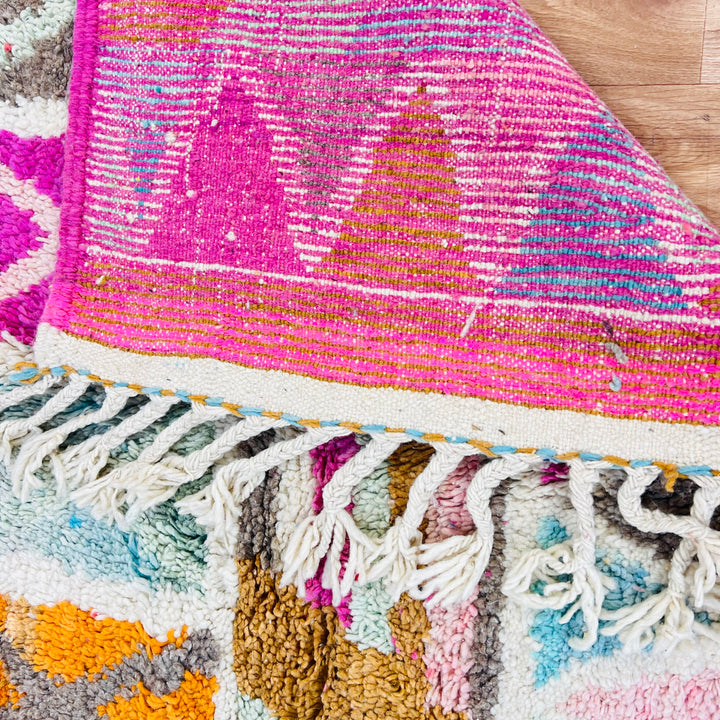Colorful handmade Moroccan rug with vibrant geometric patterns, vintage Berber design, featuring pink, turquoise, and orange hues.