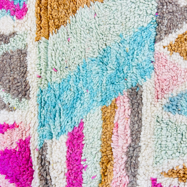 Colorful vintage Moroccan rug with geometric patterns in pink, turquoise, orange, and yellow hues on an ivory background.