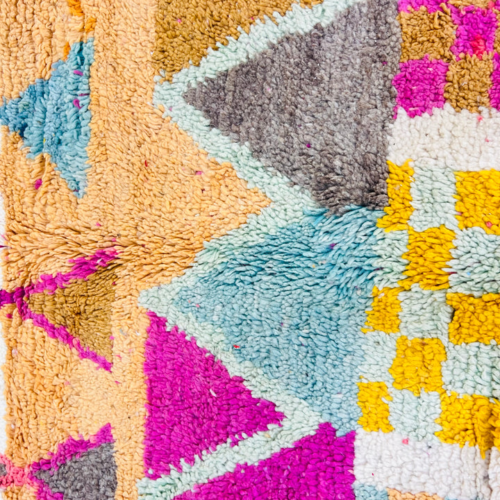 Close-up of colorful vintage Moroccan rug with geometric patterns and vibrant hues; a handcrafted wool piece by Berber artisans.