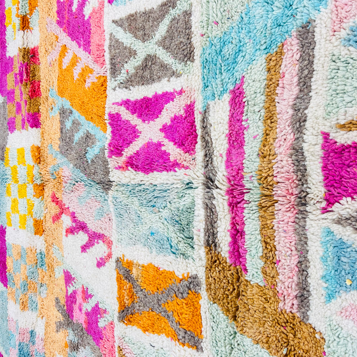 Colorful vintage Moroccan rug with geometric patterns, pink, turquoise, orange, yellow hues on ivory background. Handmade by Berber artisans.