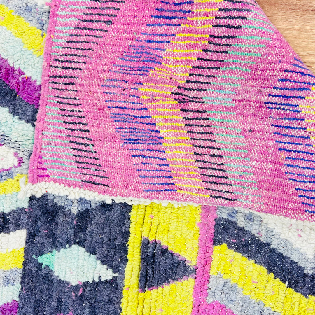 Close-up of a colorful vintage Moroccan rug with pink, yellow, and blue intricate patterns, showcasing traditional Berber craftsmanship.