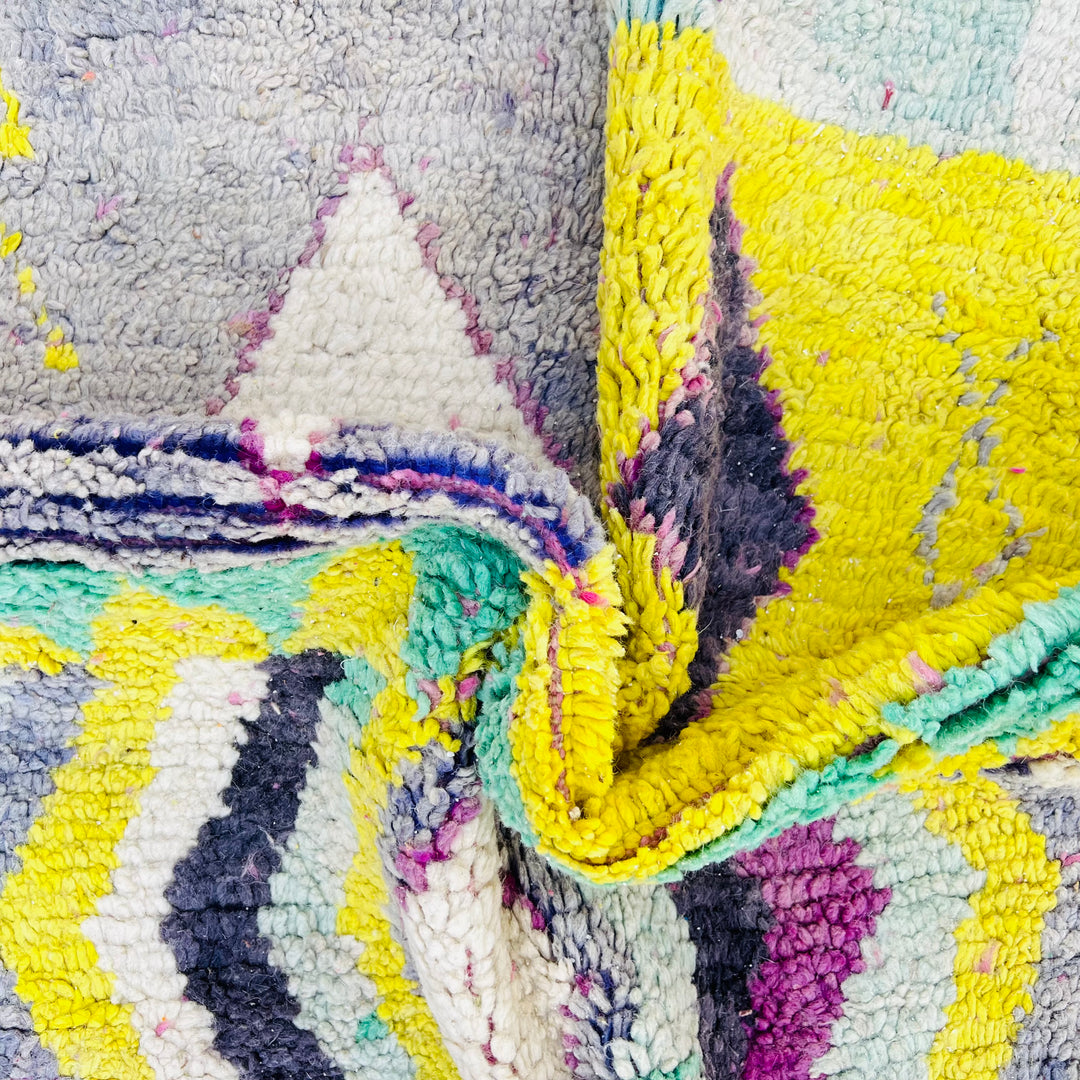 Close-up of a vintage Moroccan Berber rug with colorful diamond pattern, featuring yellow, purple, aqua, and cream shades.