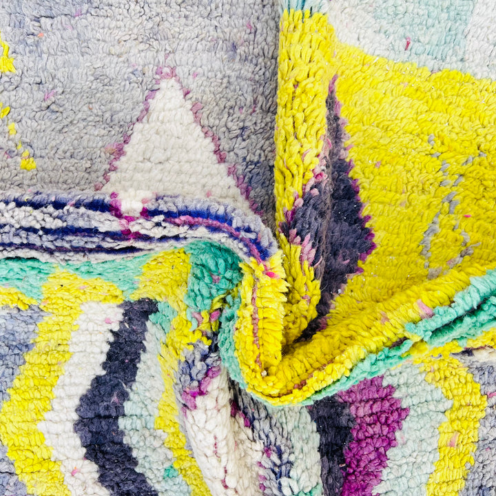 Close-up of a vintage Moroccan Berber rug with colorful diamond pattern, featuring yellow, purple, aqua, and cream shades.