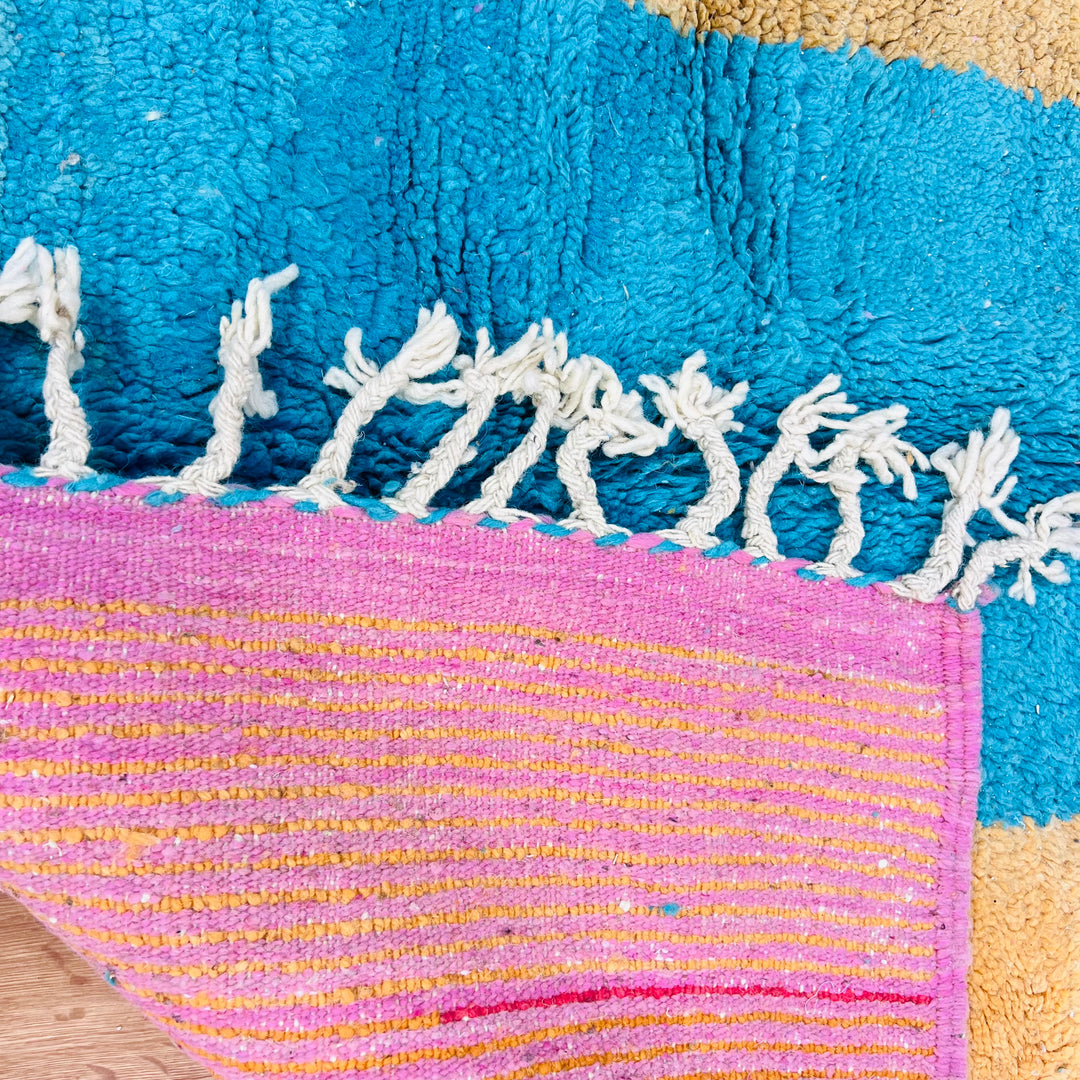 Close-up of a modern Moroccan wool rug featuring color blocks in turquoise, mustard, and a pink border. Handwoven by Berber artisans.