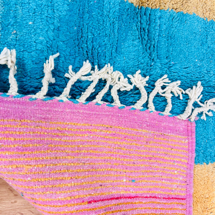 Close-up of a modern Moroccan wool rug featuring color blocks in turquoise, mustard, and a pink border. Handwoven by Berber artisans.