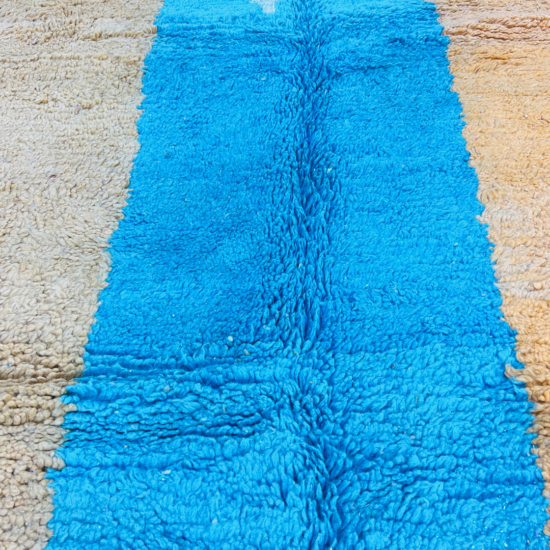 Close-up of a modern Moroccan wool rug showcasing bright turquoise and mustard color blocks with a shag texture.