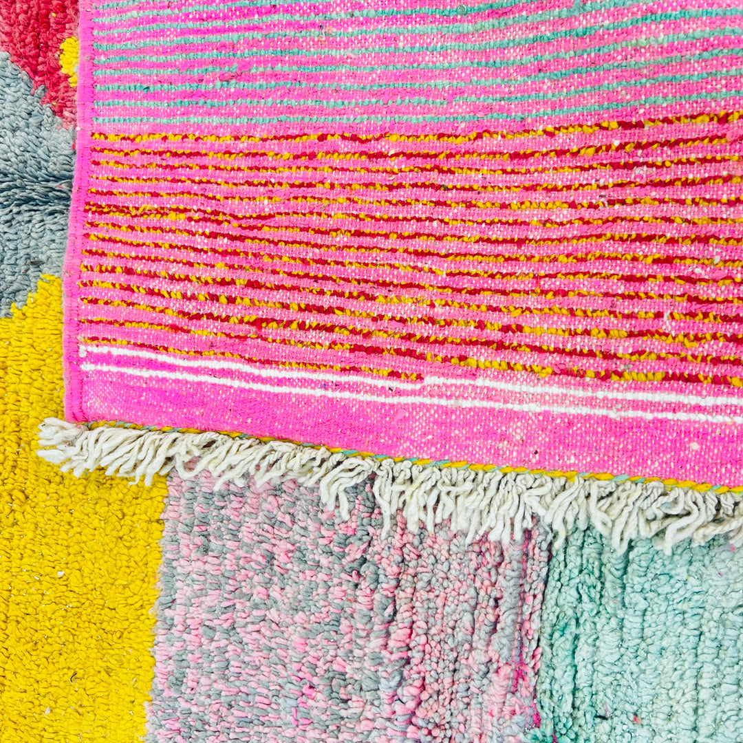 Colorful handmade Moroccan wool rug with pink, yellow, and gray triangular patterns, showcasing Berber design and artistic craftsmanship.