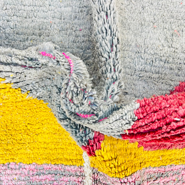 Close-up of a handmade Moroccan wool rug with vibrant color blocks in mustard yellow, soft gray, crimson red, and pastel pink.