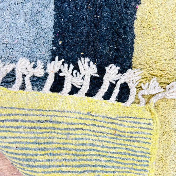 Close-up of vintage Moroccan rug with vibrant blocks in yellow, black, and grey. Handwoven fringes. Perfect for bohemian decor.