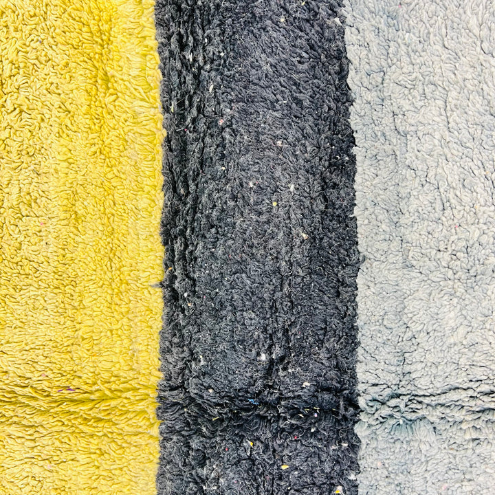 Close-up of vintage Moroccan rug with mustard yellow, black, and soft grey stripes, showcasing traditional Berber craftsmanship.