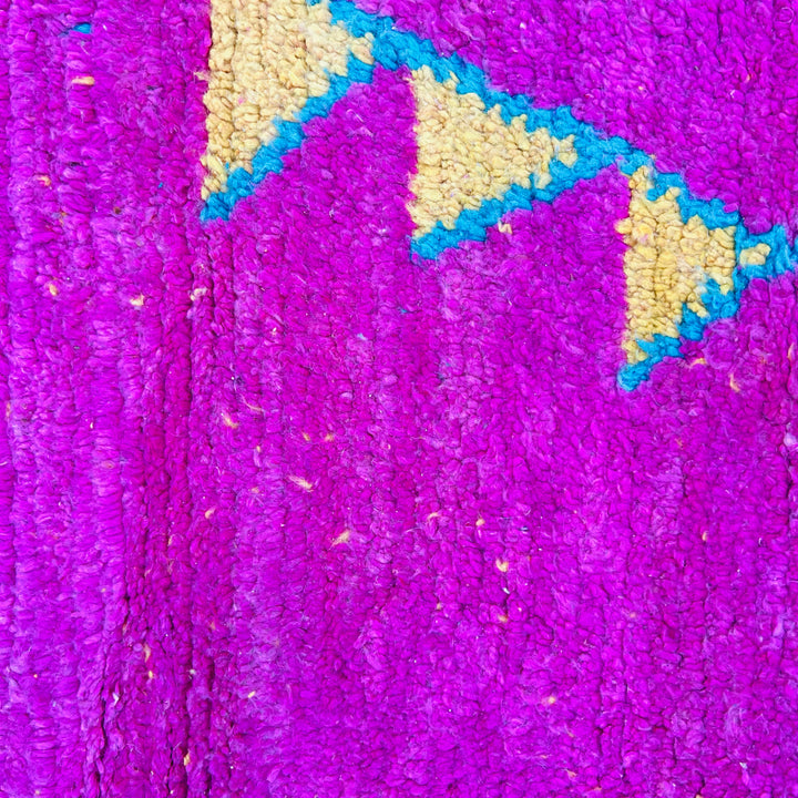 Bold pink Moroccan rug with vibrant geometric Berber motifs in blue and yellow, crafted from vintage wool. Perfect for chic interiors.