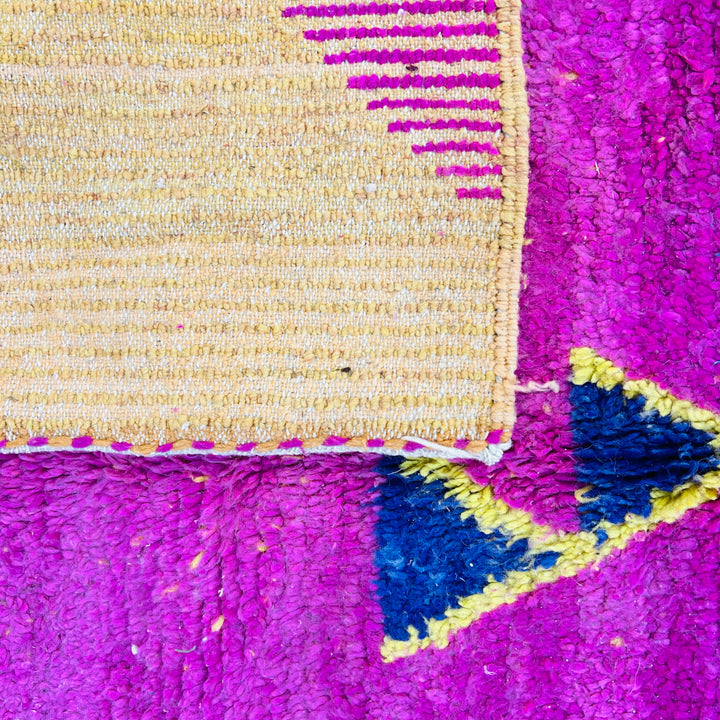 Bold pink Moroccan wool rug with vintage Berber geometric motifs in blue and yellow accents, close-up view.