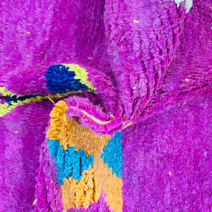 Bold pink Moroccan wool rug with vibrant magenta, blue, and yellow geometric patterns showcasing traditional Berber motifs.