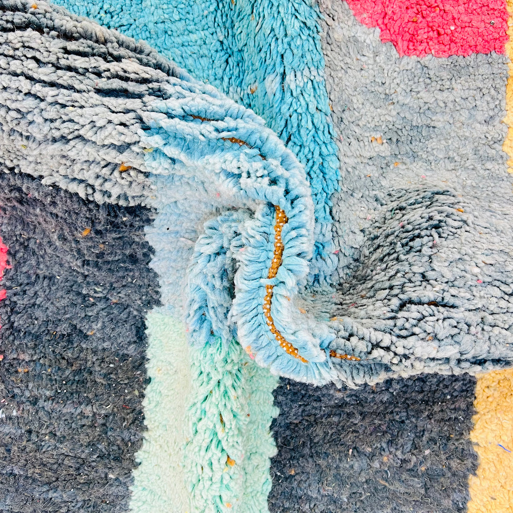 Close-up of colorful abstract vintage Moroccan rug with bold patterns in pink, yellow, turquoise, and black. Handwoven Berber design.