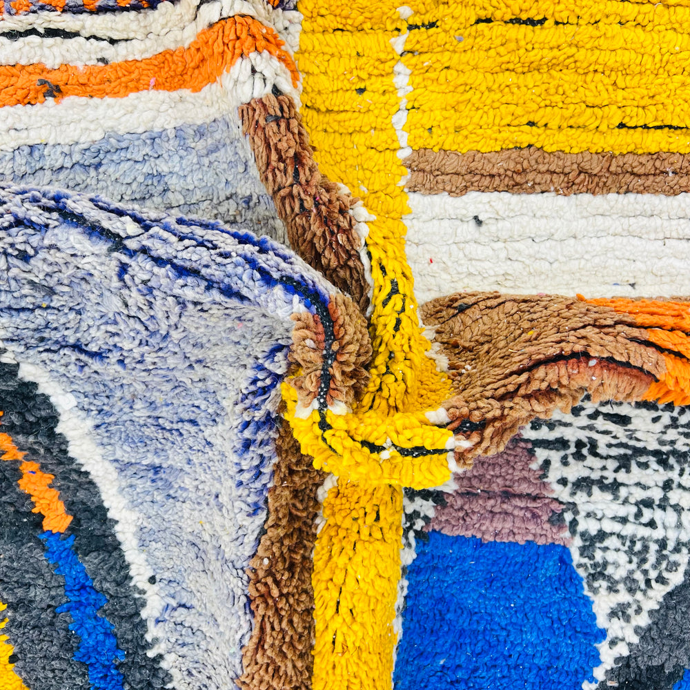 Close-up of a colorful abstract vintage Moroccan wool rug with geometric patterns in yellow, orange, blue, ivory, and charcoal.