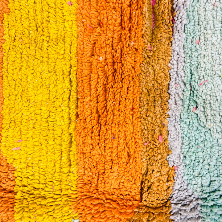 Close-up of colorful Moroccan wool rug texture with yellow, orange, and green stripes, showcasing vintage Berber craftsmanship.