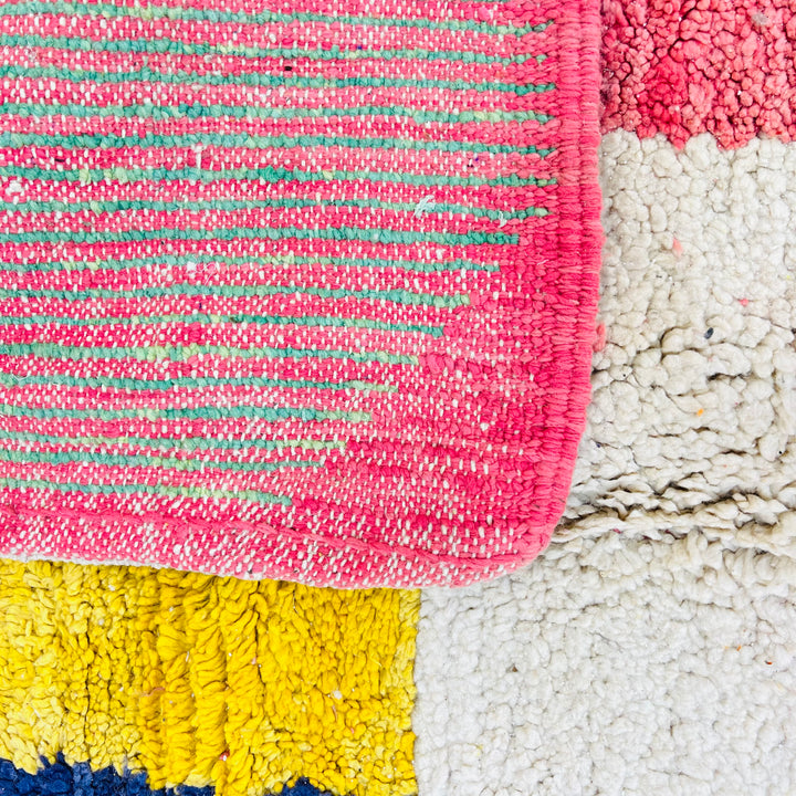Handmade colorful Moroccan wool rug with pink, yellow, and blue patches. Vintage Berber design for eclectic interiors.